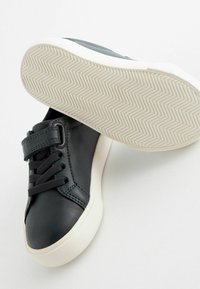 Zwarte leren sneakers met een klittenband en veters, witte rubberen zool met een visgraatpatroon, gladde textuur, ronde neus.