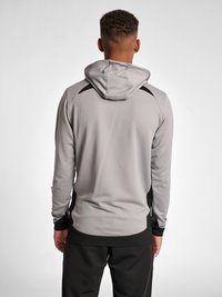 Grijze sportieve hoodie met een textuurafwerking, zwarte accenten op de schouders en een trekkoordcapuchon, gecombineerd met zwarte broek.