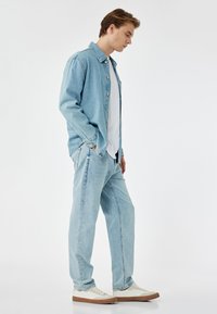 Ljusblå denimskjorta med knappar, i kombination med matchande ljusblå jeans. Vit t-shirt under och vita sneakers med ljusbruna sulor.