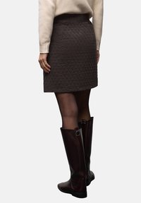 Tikkikuvioinen, tummanruskea hame, jossa on leveä, teksturoitu vyötärönauha, jossa lukee "ENJOY THE SUN", yhdistetty polven korkeisiin, kiiltäviin saappaisiin.