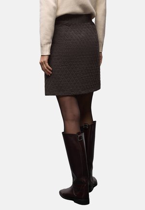 Falda acolchada de color marrón oscuro con una cinturilla ancha y texturizada que lleva la inscripción "DISFRUTA DEL SOL", combinada con botas altas hasta la rodilla y de acabado brillante.