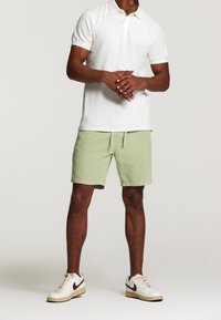 Polo blanc associé à un short en côtes vert clair et des baskets blanches avec des accents bordeaux. Design simple avec une coupe décontractée.