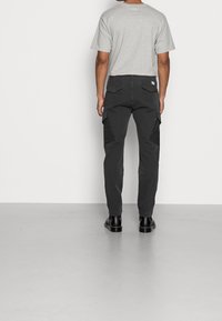 Grijze t-shirt, zwarte cargobroek met zijzakken, slim fit, gestructureerde stof, gedragen met zwarte laarzen. Gezien van achteren.