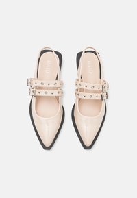 Ballerines beiges en vernis avec bouts pointus, doubles sangles cloutées, boucles en argent et semelles noires, vues de dessus.