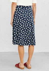 Jupe marine à pois blancs, longueur genoux, avec une taille élastique. Complétée par des sandales rouges et un haut neutre. Tissu au toucher lisse.