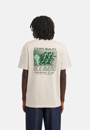 Persoon met donkere dreadlocks die een beige T-shirt draagt met een groene afbeelding en de teksten "Escape Reality" en "Running Club" op de achterkant.
