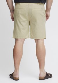 Khaki shorts laget av lett stoff, med en rett snitt, to baklommer og en kant som slutter over kneet. Brukt med brune sandaler.