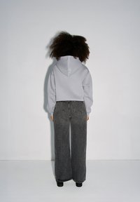 Jasnoszara bluza z kapturem z przednią kieszenią, zestawiona z ciemnoszarymi spodniami o wysokim stanie i szerokich nogawkach. Gładka tkanina i czyste linie.