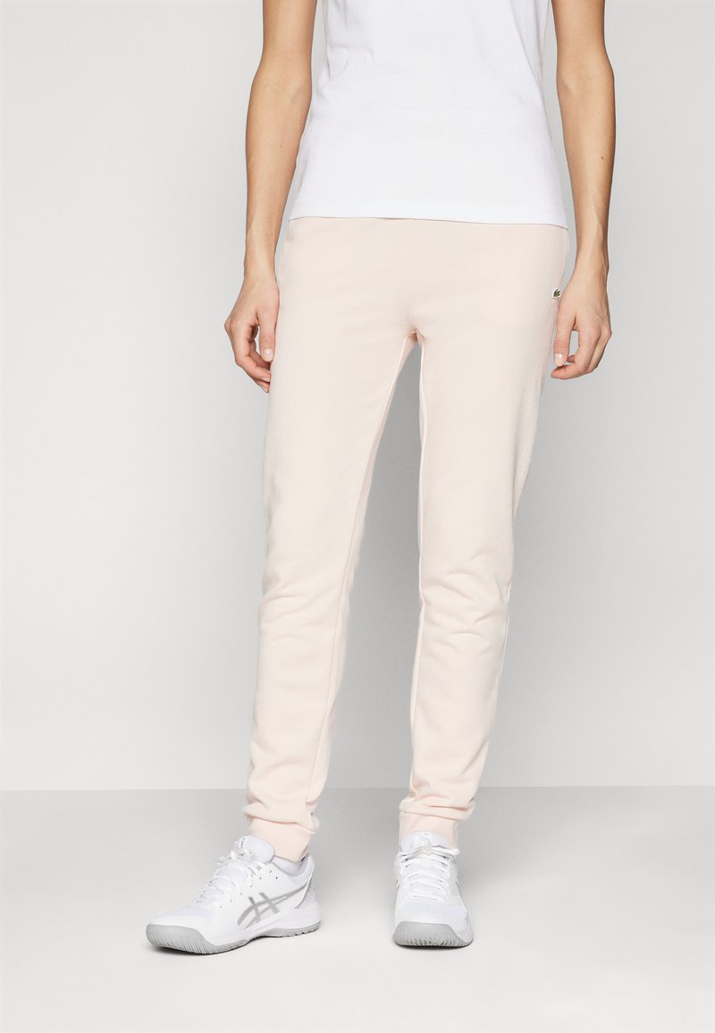 Ljust rosa sweatpants i mjukt material, med en slim fit-design, elastisk midja och en liten logodetalj på sidan.