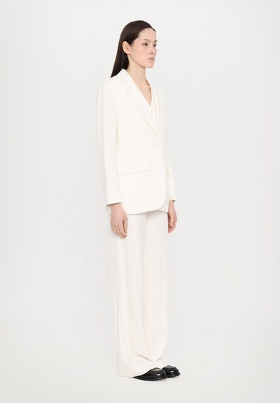 Blazer blanc ajusté à un bouton, associé à un pantalon blanc à jambes larges. Tissu lisse et design minimaliste, avec des poches latérales.