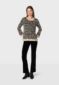 Čierny a krémový vzorovaný sveter s dlhými rukávmi a okrúhlym výstrihom, kombinovaný s priliehavými čiernymi zamatovými nohavicami a lodičkami.