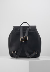 Černý batoh z koženky, kulatého tvaru, se zlatými kovovými doplňky, dvěma nastavitelnými popruhy a horním úchytem.