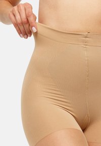 Beige tvarující prádlo s vysokým pasem, hladkým materiálem, texturovanými panely a elastickým páskem, které poskytuje těsný, přiléhavý střih.