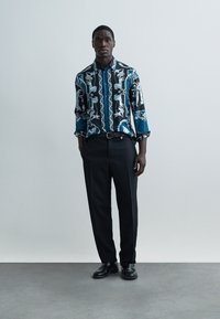 Kék-fekete ing, finom, fehér állat- és virágmintákkal díszítve; fekete nadrággal és cipővel párosítva; begombolt gallér.