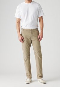 Beiga bomullschinos i rak modell, med dragkedja och knappstängning, i kombination med en enkel vit t-shirt och vita sneakers.