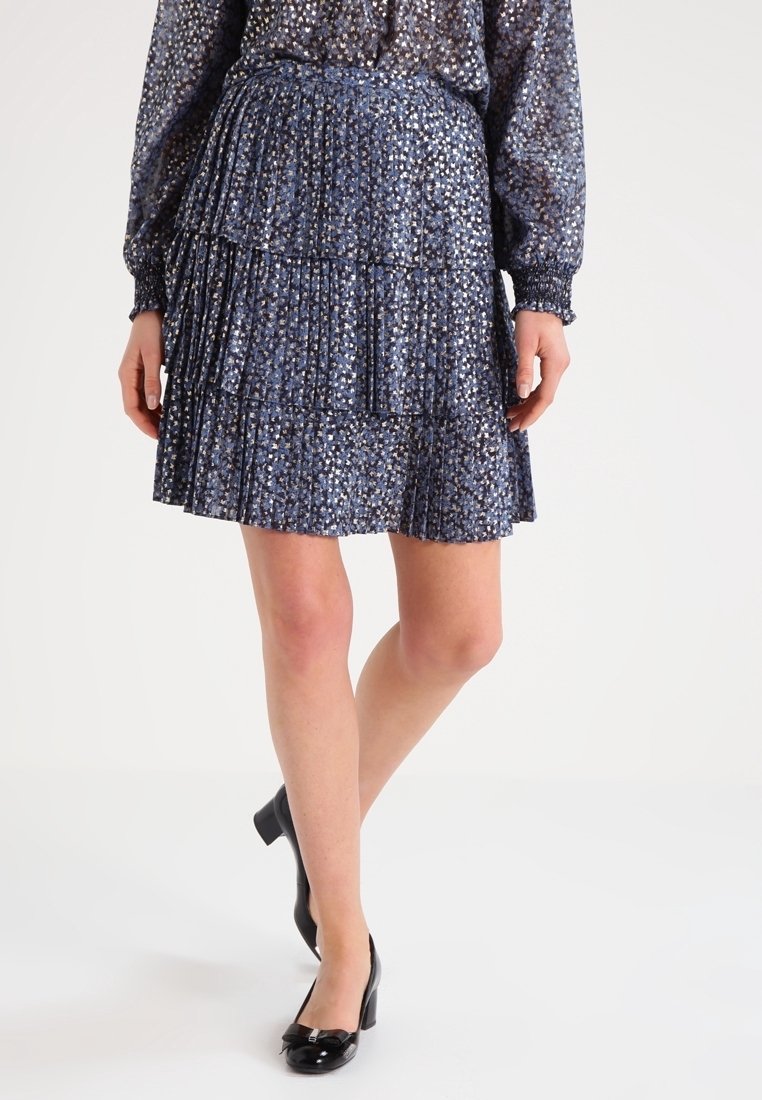 Falda azul de volantes con un sutil patrón de puntos metálicos, textura plisada y cinturilla elástica; combinada con zapatos de charol negros.