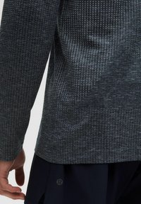 Dlhý rukáv v tmavomodrej a textúrované sivej látke, s jemným vzorom a logom, s priliehavým strihom a zaobleným lemom.