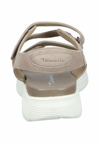 Beige suede sandals with adjustable straps, cushioned footbed, and white rubber sole. Features Tamaris branding on the heel.