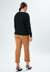 Schwarzer Pullover mit metallischen Sprenkeln, taillierte Passform, runder Ausschnitt, kombiniert mit hochgekrempelten beigen Hosen und schwarzen High-Heel-Mule.