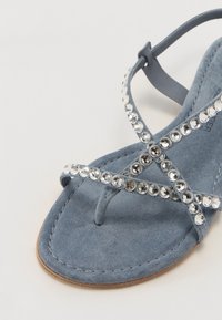 Sandale en daim bleu avec des fines lanières ornées de rhinestones argentés. Semelle plate, tige texturée et style en gantelet.