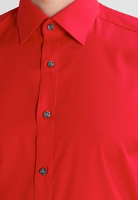 Rotes Hemd aus glattem Stoff mit Knopfleiste; verfügt über einen klassischen Kragen, sechs dunkle Knöpfe und ein minimalistisches Design ohne Muster.