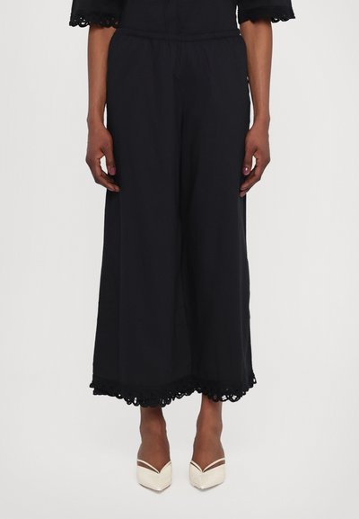Culottes negre dintr-un material ușor, cu un tiv din dantelă decorative. Asortate cu pantofi cu vârf ascuțit de culoare crem.