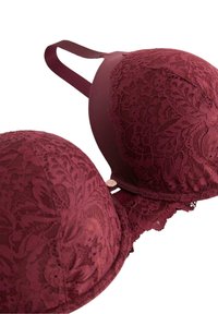 Burgundifärgad spetsbehå med formade kupor, blommönster och vågiga kanter. Har justerbara axelband och en liten dekorativ hårdvarudetalj.