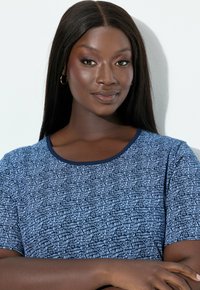 Modré tričko s krátkým rukávem a texturovaným abstraktním vzorem, kulatým výstřihem a jednobarevným tmavě modrým lemováním. Hladká látka s volným střihem.