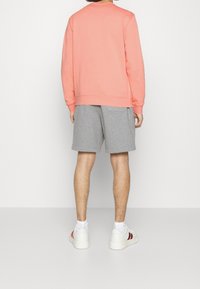 Korálová mikina s dlouhými rukávy a kulatým výstřihem, spárovaná se šedými šortkami. Obuv tvoří bílé tenisky s červenými akcenty.