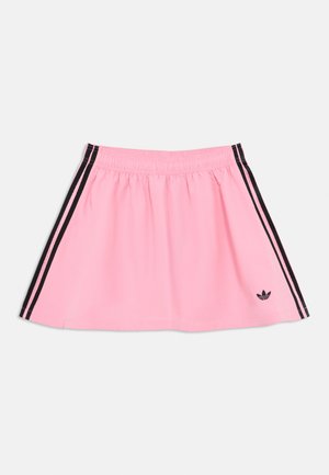 Jupe de sport rose avec une ceinture élastique, présentant des bandes latérales noires et un petit logo noir sur l'ourlet inférieur. Texture de tissu lisse.