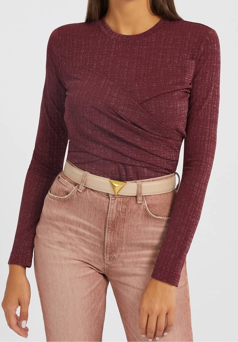 Bordeauxfarbenes Langarmshirt mit strukturiertem Finish und gewickeltem Design. Kombiniert mit hellrosafarbenen, hochgeschnittenen Jeans und einem cremefarbenen Gürtel mit goldfarbener Dreiecksschnalle.
