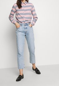 Chemise à rayures boutonnée rose et grise, associée à un jean bleu clair à jambes droites. Des mocassins noirs complètent la tenue.
