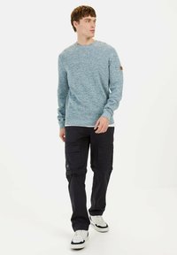 Light blue textured sweater with a round neckline paired with black cargo pants featuring multiple pockets. Model also wears white sneakers.
