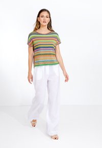 Top lavorato a maglia multicolore con motivi geometrici, maniche corte e scollo rotondo, abbinato a pantaloni larghi in lino bianco.