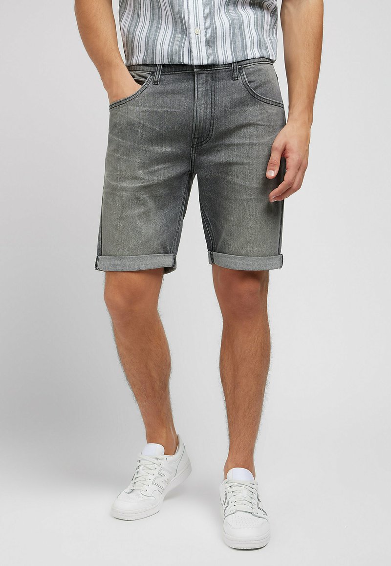 Pantalones cortos de mezclilla gris con puños doblados, que cuentan con bolsillos frontales y una textura suave. Combinados con zapatillas deportivas blancas.