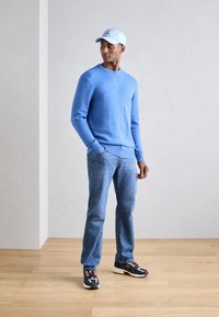 Hellblauer Pullover, Jeans und mehrfarbige Sneaker. Der Pullover hat einen Rundhalsausschnitt und gerippte Bündchen, während die Sneaker ein Logo aufweisen.