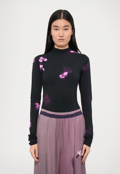 Zwarte top met lange mouwen en paars bloemenprint, hoge halslijn, gecombineerd met een vloeiende, lavendelkleurige rok met een zachte textuur en elastische tailleband.