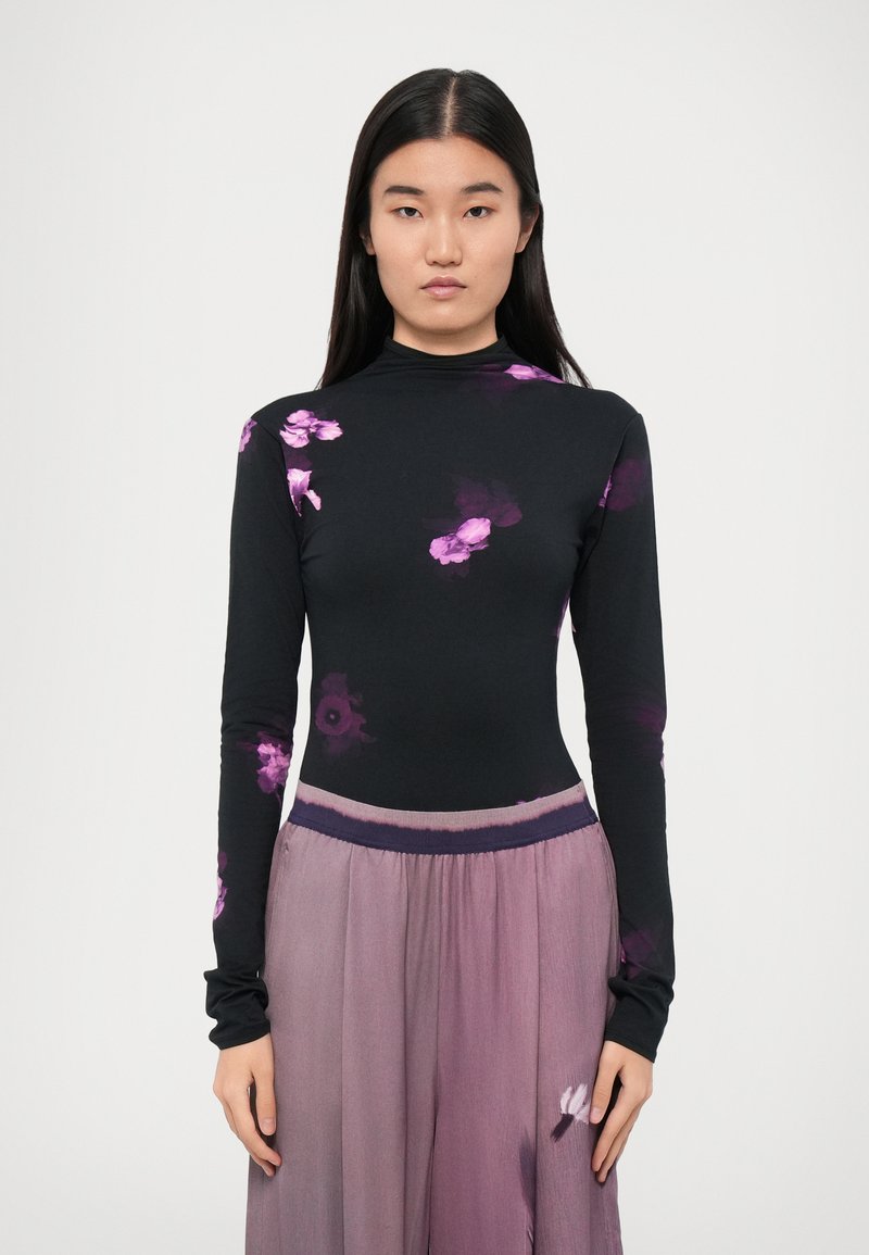 Long-sleeve black top with purple floral print, high neckline, paired with a flowing, lavender skirt featuring a soft texture and elastic waistband.