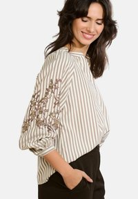 Blusa a righe in crema e marrone chiaro con colletto alla mandarino, caratterizzata da ricami floreali decorativi sulle maniche e un fit rilassato.