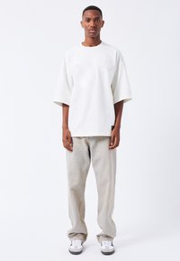 Bílé oversized tričko s krátkým rukávem, kombinované se světle šedými rovnými džíny a černobílými teniskami.