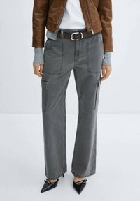 Pantalons cargo gris à jambes larges, dotés de multiples poches et d'une taille haute. Portés avec une ceinture noire et accentués par des talons aiguilles noirs.