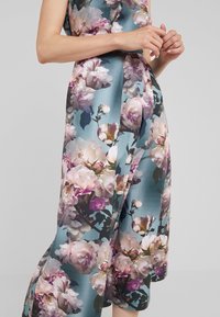 Blommönstrad klänning i tealtyg, med stora rosa och vita rosor, med en mjuk, lätt textur och en figurnära silhuett.