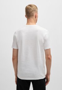 Witte T-shirt met korte mouwen, ronde hals, gladde katoenen stof, eenvoudig ontwerp, zichtbare stiksels, gedragen met donkere broek.