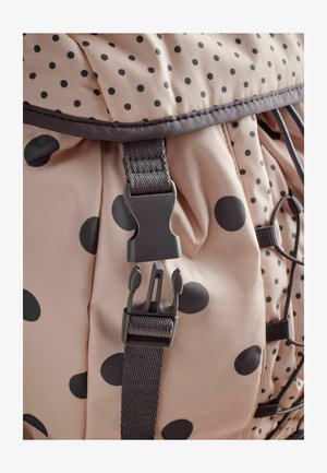 Helles pinken Stoff-Rucksack mit schwarzen Punkten; verfügt über einen Kunststoffverschluss und verstellbare Nylonriemen, mit einem Zugverschluss oben.
