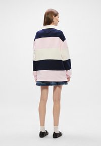 Πουλόβερ με χρώματα σε ροζ, ναυτικό και κρεμ, με χαλαρή εφαρμογή, διαθέτει μακριά μανίκια και V-λαιμόκοψη; συνδυάζεται με τζιν φούστα.