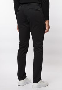 Zwarte broek met een gladde textuur, slim fit ontwerp en twee achterzakken. Graagd met witte sneakers, wat een casual stijl uitstraalt.