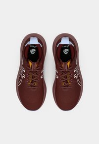 Burgundy juoksutossut, joissa on teksturoitu päällinen, valkoinen logo ja erottuvat keltaiset reikähakemukset. Varustettu pehmeällä pohjalla ja tasaisilla nauhoilla.