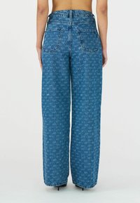 Weite blaue Denim-Jeans mit einem verblassten Muster, hoher Taille und zwei Gesäßtaschen. Der Stoff hat eine strukturierte Haptik und einen geraden Schnitt.