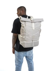 Beige színű roll-top hátizsák, textúrált anyagból készült, állítható pántokkal, elasztikus bungee zsinórral és több cipzáras rekesszel a rendezett tárolás érdekében.