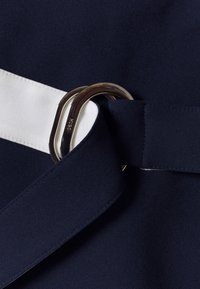 Marineblauer Stoff mit einem weißen Streifen, versehen mit einer silbernen Metallbindung und einer glatten Textur, die ein stromlinienförmiges Designelement schafft.